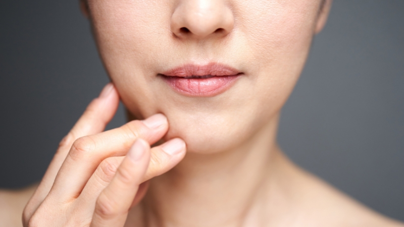 Krupan prikaz donjeg dela lica žene koja dodiruje obraz u području nazolabijalnih bora