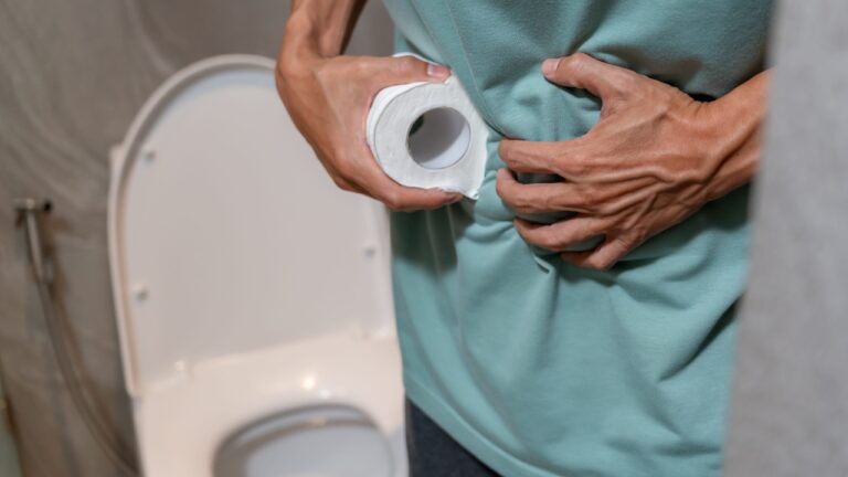 Osoba u toaletu drži rolnu papira i stomak zbog nelagodnosti.